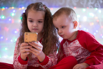 children in Christmas pajamas playing smartphone