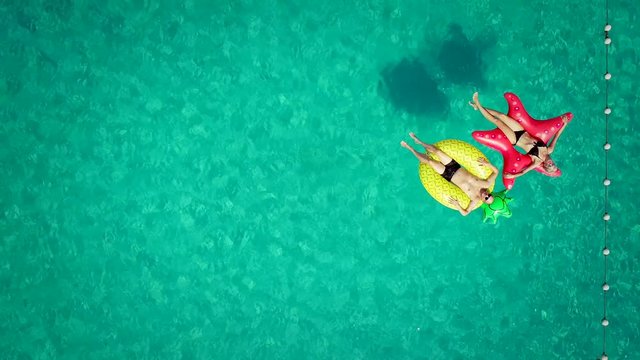Aerial view of man and woman floating by string buoy on inflatable mattresses in clear blue sea.