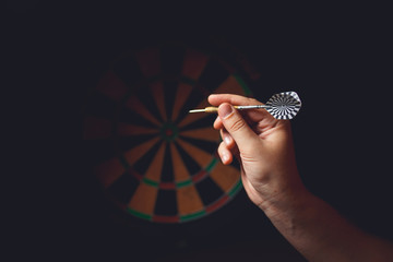 Hand holding a dart aiming at the target - business targeting, aiming, focus concept.