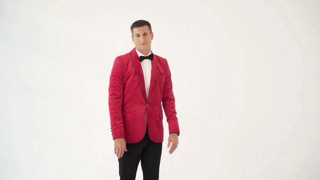 showman in a red jacket with a bow tie is circling around himself with openarmed hands in different sides on a white background