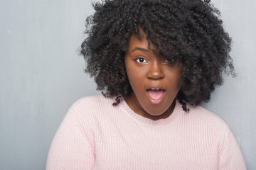 Young african american plus size woman over grey grunge wall wearing winter sweater afraid and shocked with surprise expression, fear and excited face.