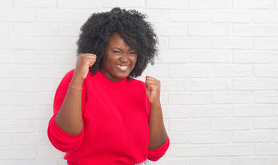 Young african american plus size woman over white brick wall very happy and excited doing winner...