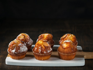 Freshly baked vanilla muffins with sugar powder, served on wooden board. Horizontal. Top view. Copy space, Dark Background.