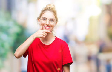 Young beautiful blonde woman wearing red t-shirt and glasses over isolated background looking confident at the camera with smile with crossed arms and hand raised on chin. Thinking positive.