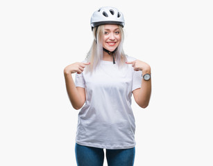 Young blonde woman wearing cyclist security helmet over isolated background looking confident with smile on face, pointing oneself with fingers proud and happy.