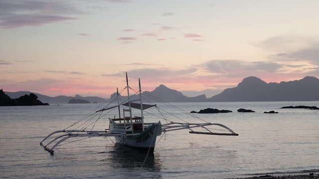 Slow motion shot of traditional filipino bangka boat on calm waters at dusk with pink and orange sky