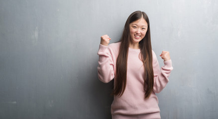 Young Chinese woman over grey wall very happy and excited doing winner gesture with arms raised, smiling and screaming for success. Celebration concept.