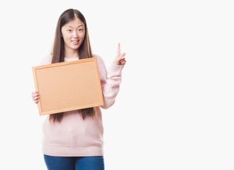 Young Chinese woman over isolated background holding corkboard surprised with an idea or question pointing finger with happy face, number one