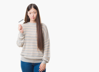 Young Chinese woman over isolated background holding credit card with a confident expression on smart face thinking serious