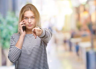 Young caucasian woman showing smartphone screen over isolated background pointing with finger to the camera and to you, hand sign, positive and confident gesture from the front
