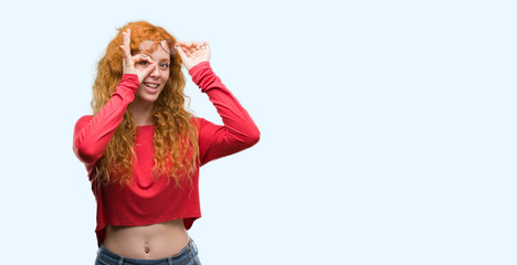 Young redhead woman wearing glasses with happy face smiling doing ok sign with hand on eye looking through fingers