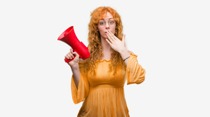 Young redhead woman holding megaphone cover mouth with hand shocked with shame for mistake, expression of fear, scared in silence, secret concept