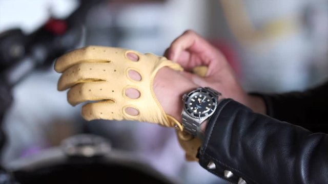 A biker puts on vintage yellow leather knuckle less gloves wearing a vintage watch.