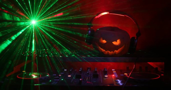 Halloween pumpkin on a dj table with headphones on dark background with copy space. Happy Halloween festival decorations and music concept. Empty space. Selective focus