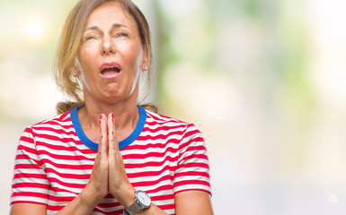 Middle age senior hispanic woman over isolated background begging and praying with hands together with hope expression on face very emotional and worried. Asking for forgiveness. Religion concept.