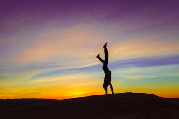 Fototapeten Silhouette of woman doing hand stand on sand dune during the sunset © Boy