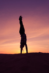 Silhouette of woman doing hand stand on sand dune during the sunset