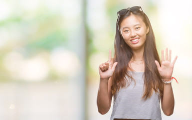 Young asian woman wearing sunglasses over isolated background showing and pointing up with fingers number seven while smiling confident and happy.