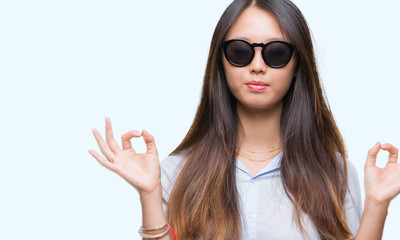 Young asian woman wearing sunglasses over isolated background relax and smiling with eyes closed doing meditation gesture with fingers. Yoga concept.