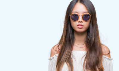 Young asian woman wearing sunglasses over isolated background with serious expression on face. Simple and natural looking at the camera.