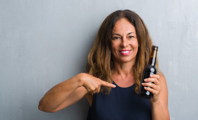 Fototapeta na wymiar Middle age hispanic woman standing over grey grunge wall holding beer bottle with surprise face pointing finger to himself