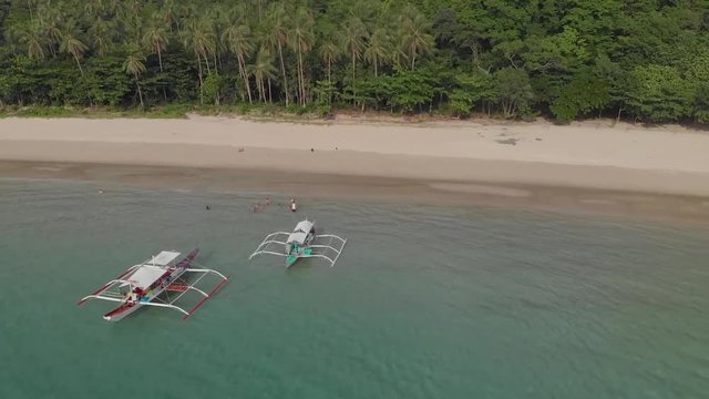 Aerial drone shot away from people swimming, near a parked paraw boat, at a beach, in a turquoise lagoon, on a sunny evening, in the archipelago of Palawan island, El Nido, Philippines, Asia