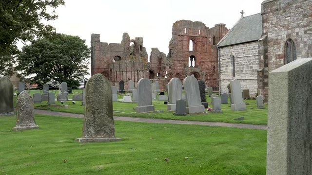Cold windy day at a church cemetery with the ruins on the Lindisfarne Priory in the background on Holy Island a tidal island off the northeast coast of England.