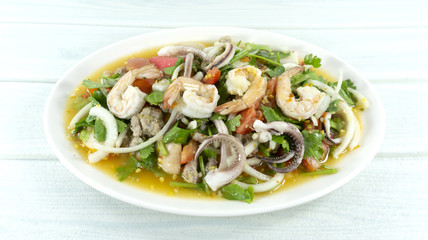 spicy seafood shrimp and squid salad in white plate Thai foods. white wooden backdrop. Top view. Copy Space.