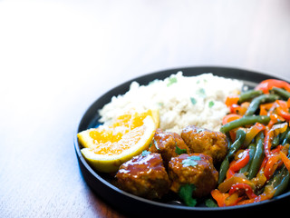 Close up photograph of a low carb meatball dinner with side of mashed cauliflower and string beans and red pepper garnished with orange slices and cilantro served on a black plate with wood background