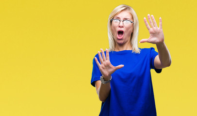 Young beautiful blonde woman wearing glasses over isolated background afraid and terrified with fear expression stop gesture with hands, shouting in shock. Panic concept.