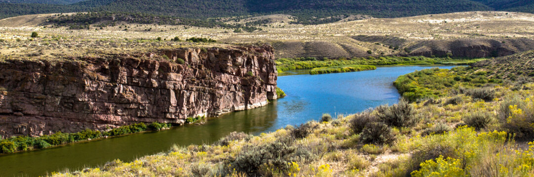Panorama of the Green River as it passes by red-brown rock cliffs, wetlands, wide prairies, and mountains in Browns Park National Wildlife Refuge in northwestern Colorado