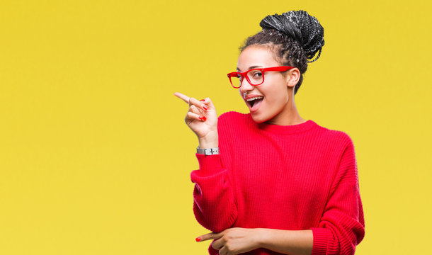 Young braided hair african american girl wearing sweater and glasses over isolated background with a big smile on face, pointing with hand and finger to the side looking at the camera.