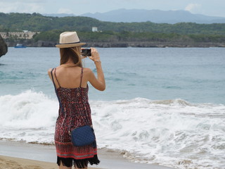 young woman in hat on the beach holding a camera