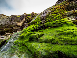 Beautiful waterfall over mossy stones in the Cove of Tintagel in Cornwall