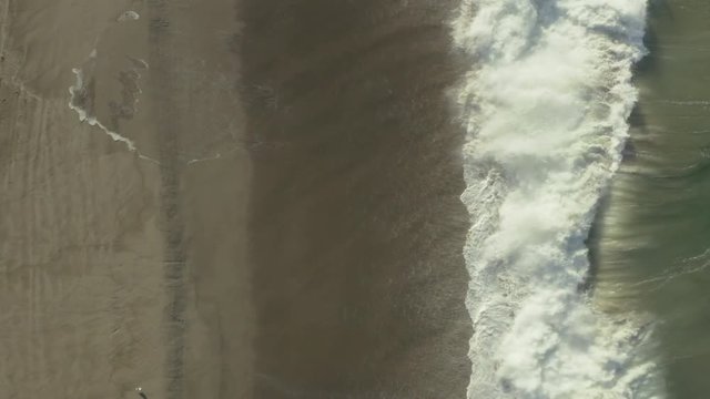 Birdseye view of waves crashing against rocks on the beach.