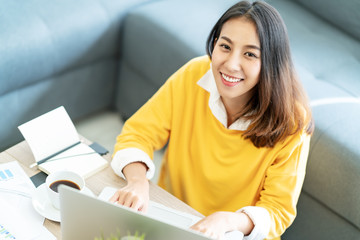 Young attractive happy asian female student sitting at living room floor smiling and looking up at...