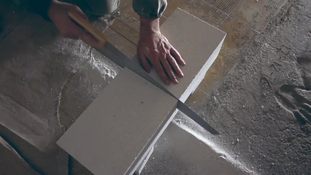Man sawing some white building blox with a handsaw.