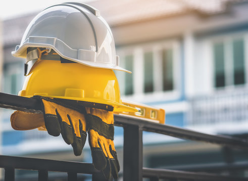 White and yellow helmet  with gloves are placed on steel house fence.