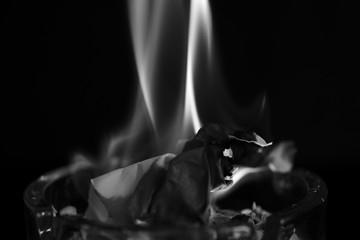 A piece of paper burning in a glass ashtray close up. Black and white