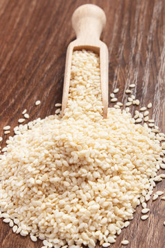 Heap of sesame seeds with wooden scoop on board