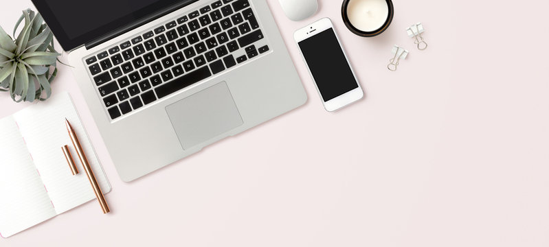 modern header / hero image or banner with laptop computer, smartphone, air plant, open notebook and feminine accessories on a bright blush background, home office scene, flat lay / top view