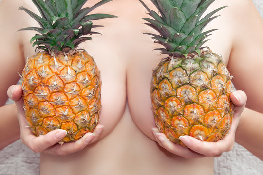 A young woman holds pineapples at her breasts. Bra from pineapples. Close-up.
