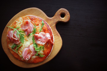 Pizza with smoked ham and rucola on black background. Top view