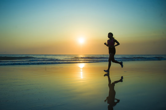 silhouette of young happy and attractive African American runner woman exercising in running fitness workout at beautiful beach jogging and enjoying sunset