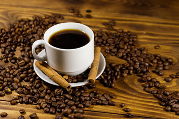 Cup of coffee, roasted coffee beans and cinnamon sticks on wooden table