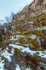 Fototapeta na wymiar The cascade slope of the rock with mosses and icicles