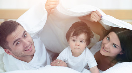 Happy family posing under a duvet while looking at the camera