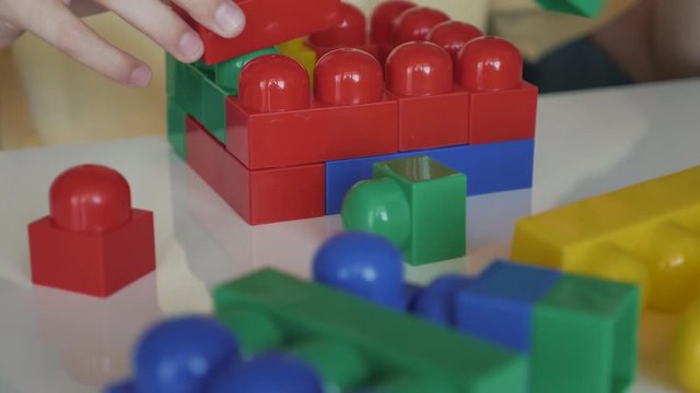 Close-up of the boy's hand collecting the developing designer blocks sitting at the white table. The concept of a happy childhood