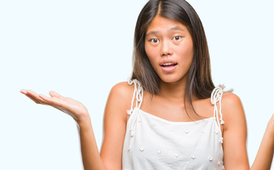 Young asian woman over isolated background clueless and confused expression with arms and hands...