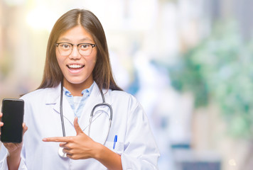 Young asian doctor woman holding smartphone over isolated background very happy pointing with hand and finger